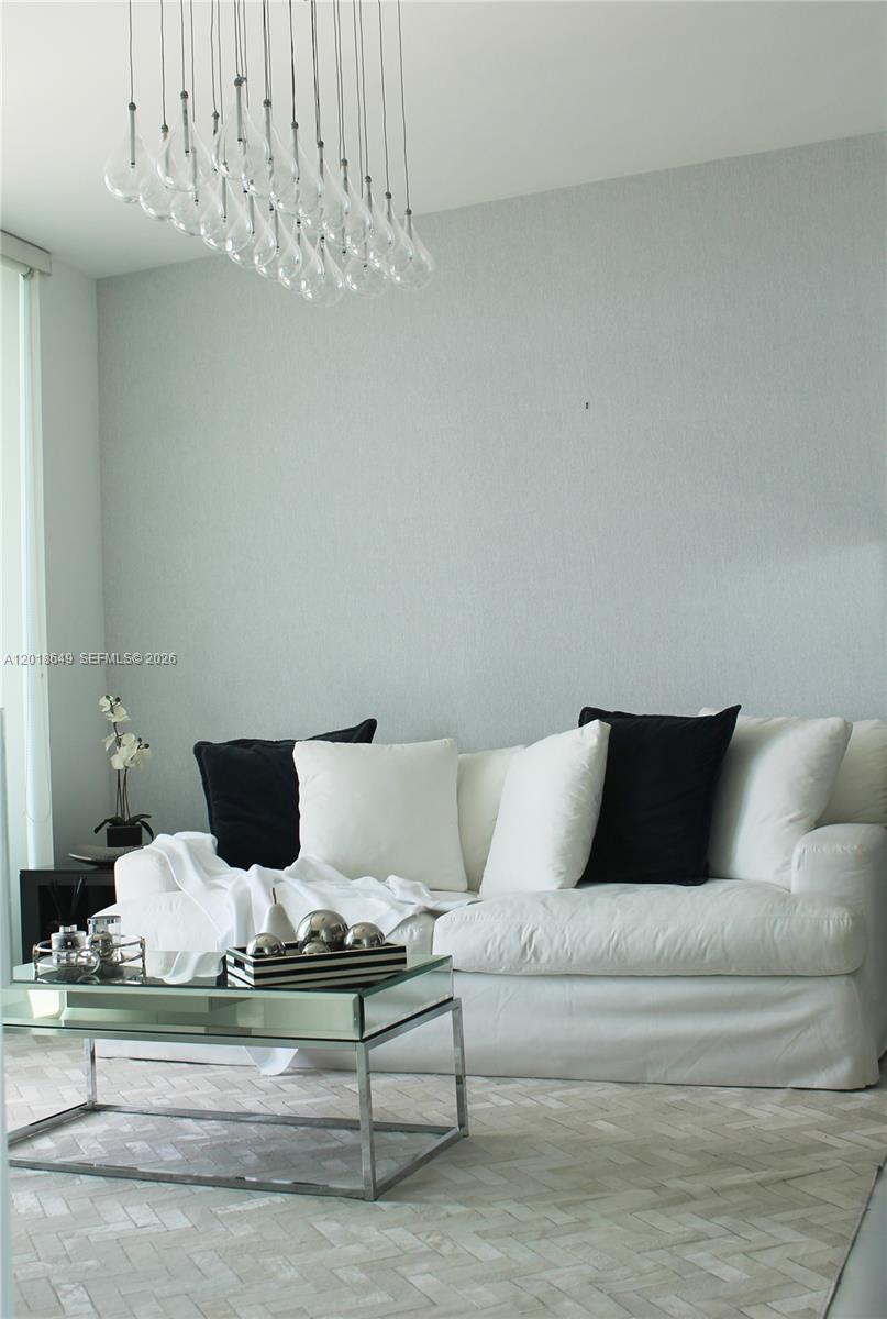 A living room features a white sofa with black pillows beneath a modern glass chandelier — 900 Biscayne Blvd # 3207, Miami FL 33132, MIAMI, FL