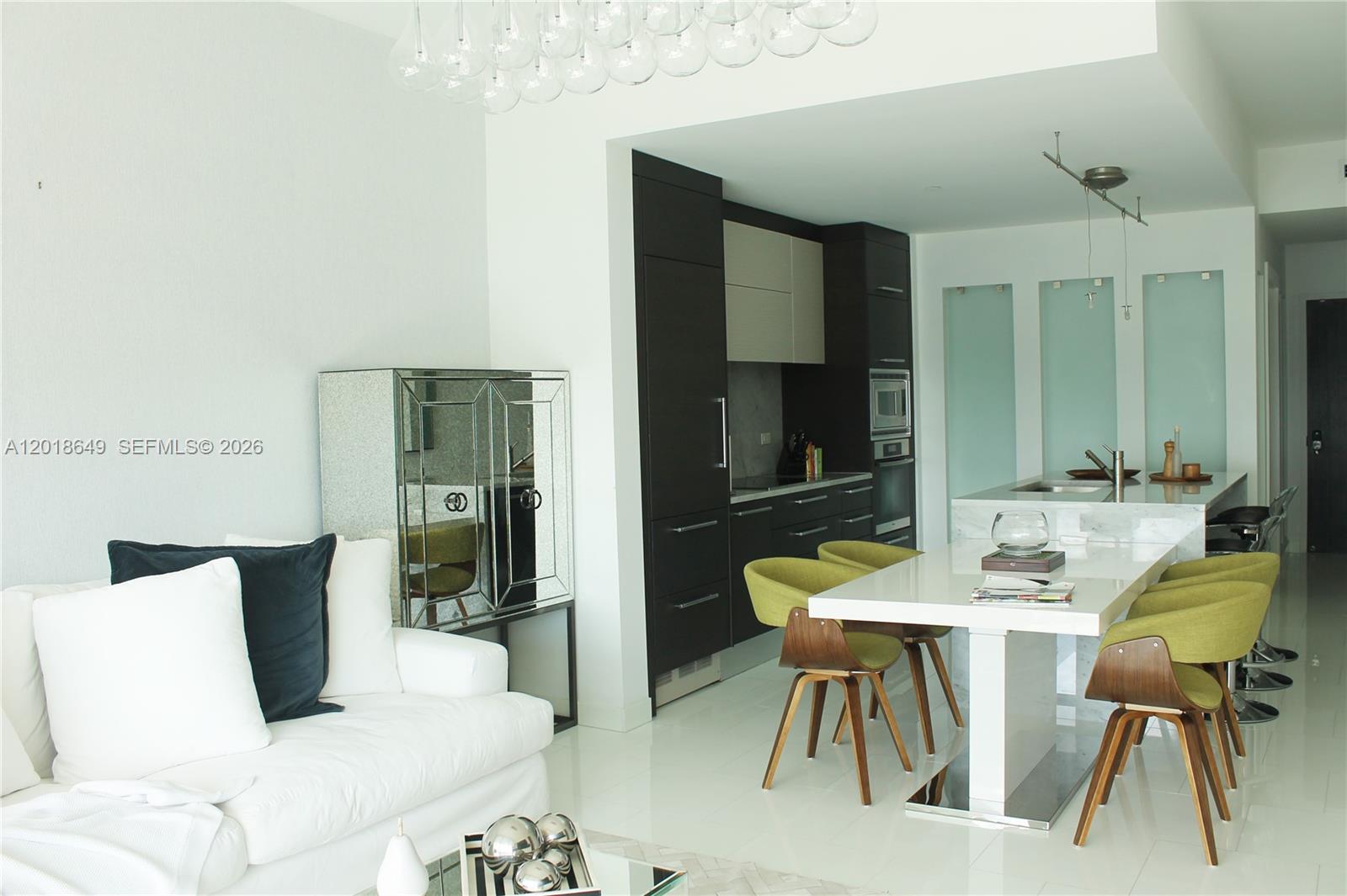 A modern kitchen and dining area features dark cabinetry, a white island, and green chairs — 900 Biscayne Blvd # 3207, Miami FL 33132, MIAMI, FL