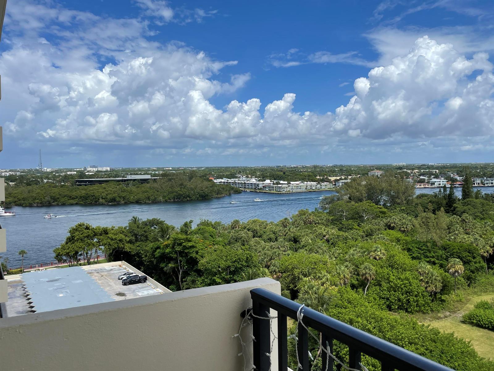 A high-angle view from a balcony overlooking a waterway, lush greenery, and distant buildings — 2121 N Ocean Boulevard # 1204e, Boca Raton FL 33431, BOCA RATON, FL