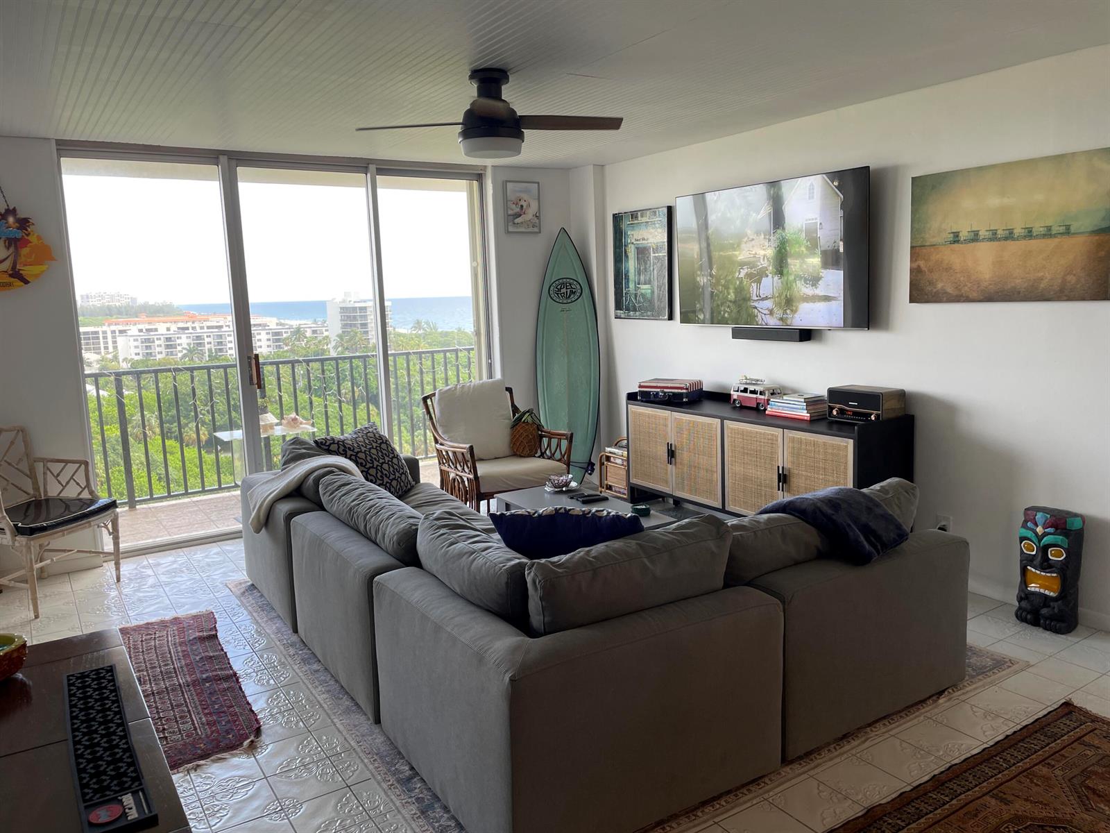 A living room with a grey sectional, surfboard decor, and a balcony overlooking the ocean — 2121 N Ocean Boulevard # 1204e, Boca Raton FL 33431, BOCA RATON, FL