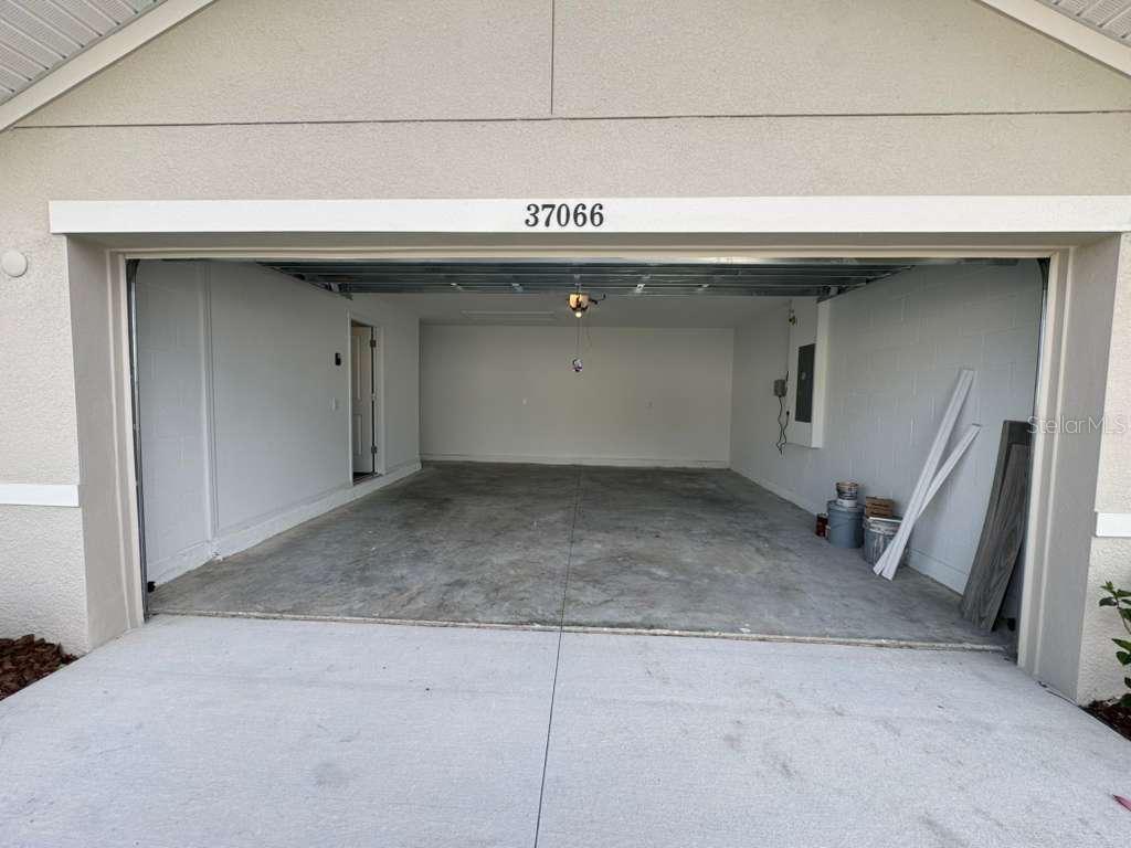 An empty two-car garage with concrete floors, white block walls, and an open overhead door — 37066 KINGS CROWN DRIVE, ZEPHYRHILLS, FL
