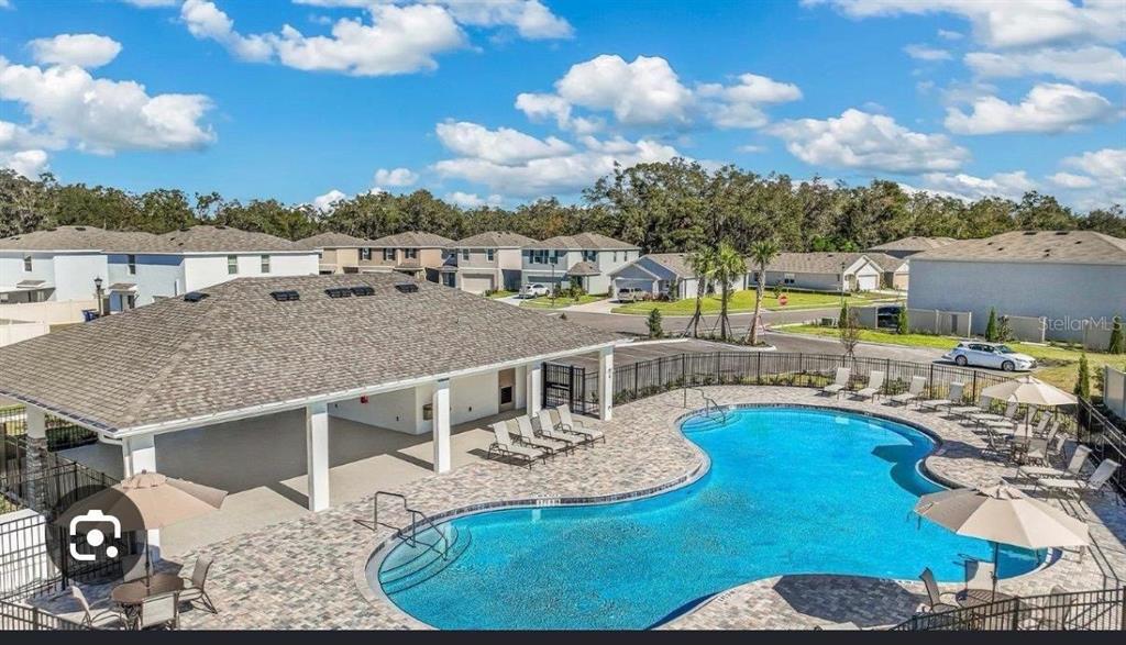 An aerial view of a community swimming pool with a covered patio and lounge chairs — 37066 KINGS CROWN DRIVE, ZEPHYRHILLS, FL