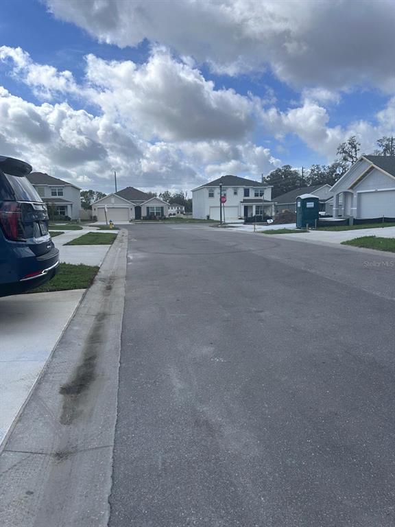 A residential street features suburban houses, a parked vehicle, and a portable toilet — 37066 KINGS CROWN DRIVE, ZEPHYRHILLS, FL