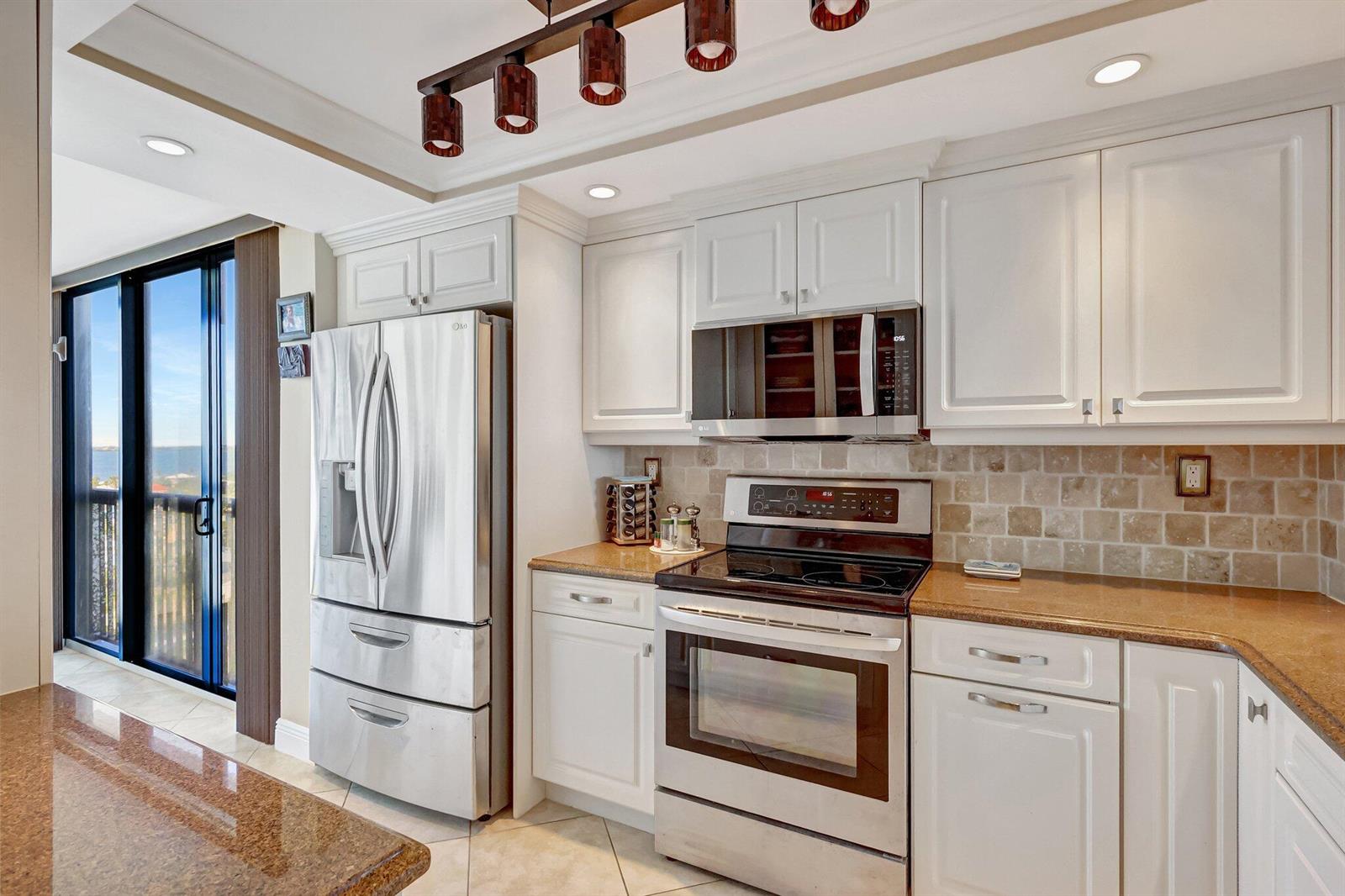 A kitchen features white cabinets, stainless steel appliances, granite countertops, and a stone tile backsplash — 10680 S Ocean Drive # 901, Jensen Beach FL 34957, JENSEN BEACH, FL