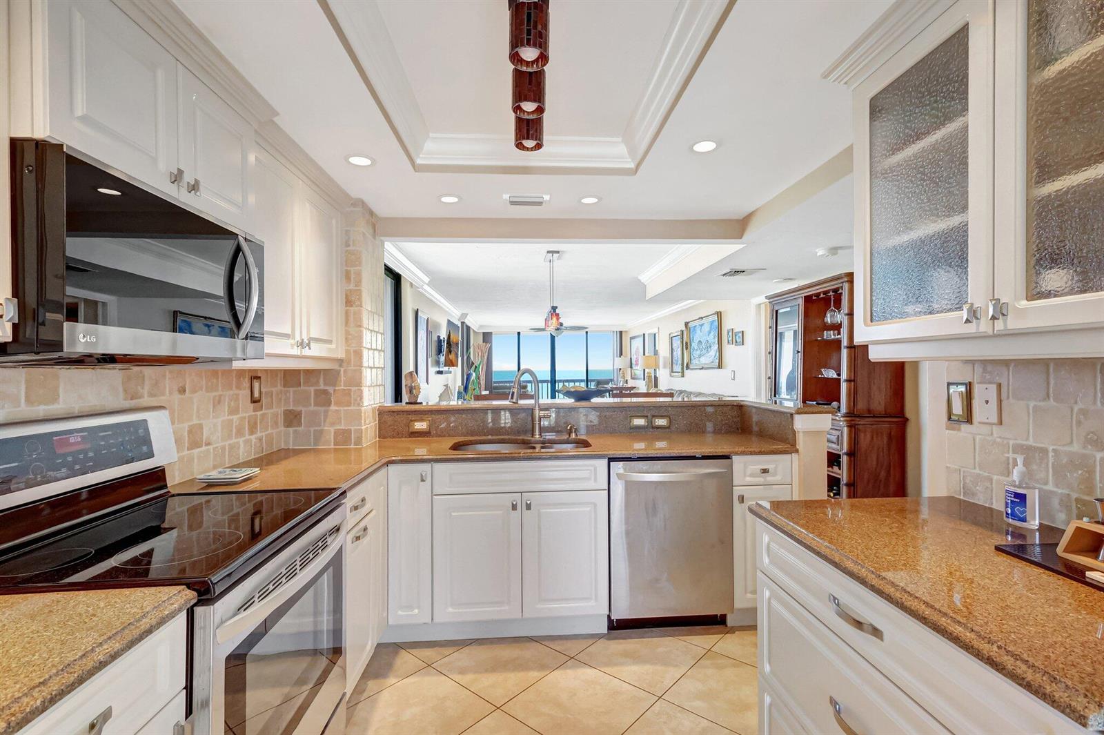 A kitchen with white cabinets, granite countertops, and stainless steel appliances overlooks a living area — 10680 S Ocean Drive # 901, Jensen Beach FL 34957, JENSEN BEACH, FL