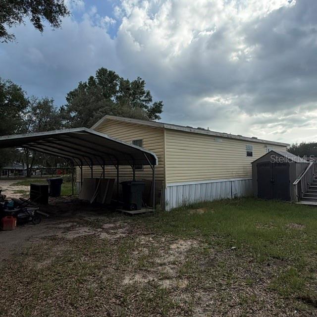 A mobile home exterior features a metal carport, a storage shed, and a grassy yard — 7651 E DERBY OAKS DRIVE, FLORAL CITY, FL