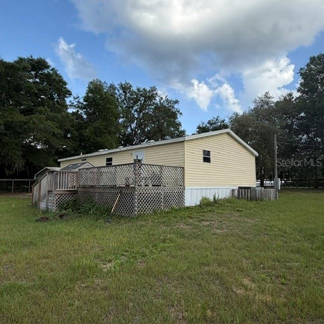 A yellow mobile home with a wooden deck sits in a grassy field — 7651 E DERBY OAKS DRIVE, FLORAL CITY, FL