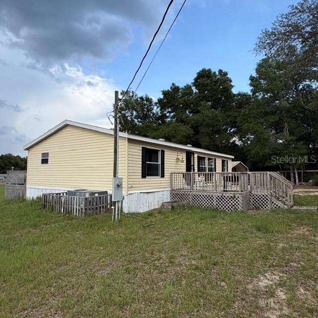 A yellow manufactured home with a wooden deck and lattice skirting sits on a grassy lot — 7651 E DERBY OAKS DRIVE, FLORAL CITY, FL