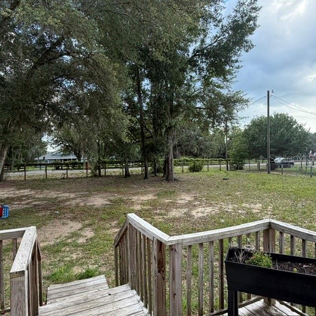 A wooden deck overlooks a grassy backyard with mature trees and a fenced perimeter — 7651 E DERBY OAKS DRIVE, FLORAL CITY, FL
