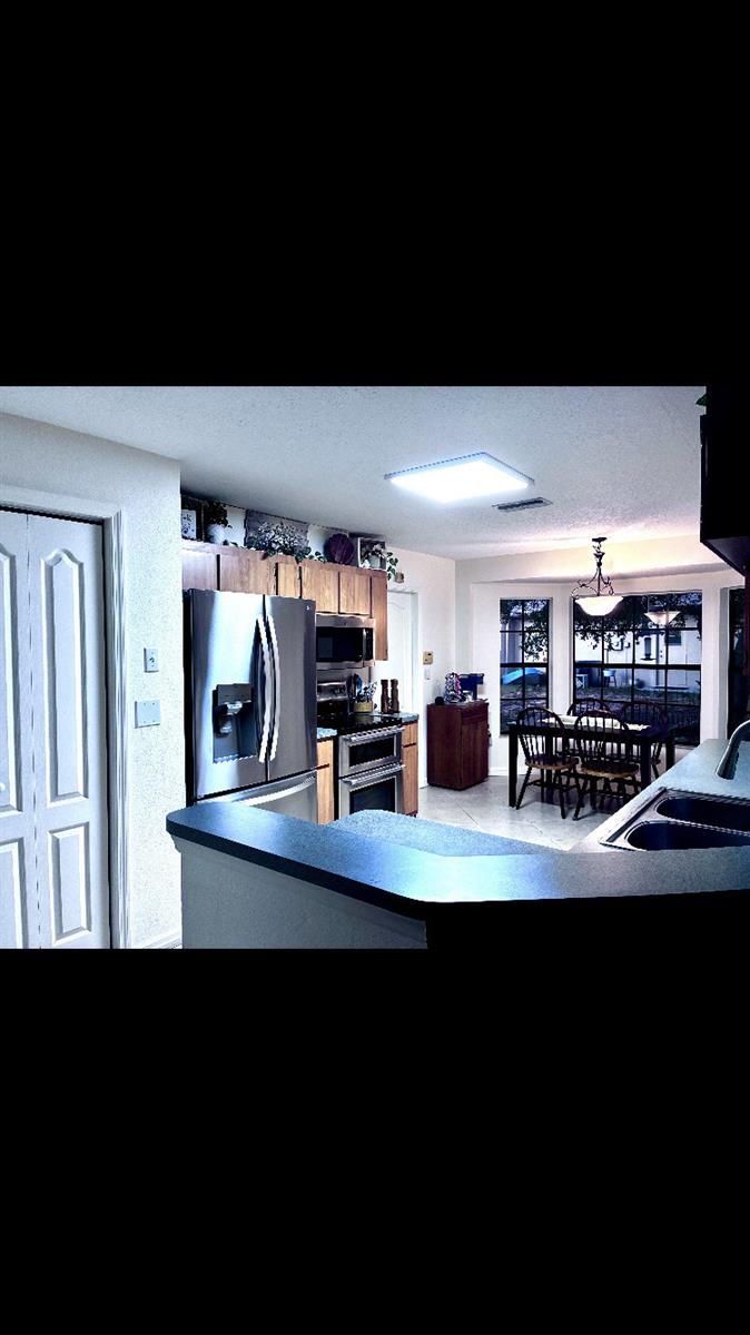 A kitchen with stainless steel appliances, wood cabinets, and an adjacent dining area with windows — 14050 Brighton Street, Spring Hill FL 34609, SPRING HILL, FL