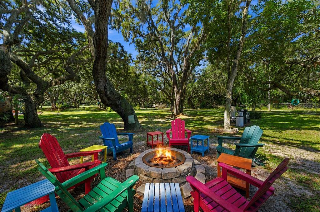 A stone fire pit surrounded by colorful Adirondack chairs sits in a grassy, tree-filled yard — 5710 MOUNT OLIVE ROAD, POLK CITY, FL
