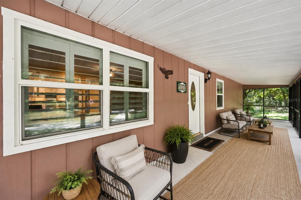 A covered porch features brown vertical siding, a white front door, and outdoor seating furniture — 5710 MOUNT OLIVE ROAD, POLK CITY, FL