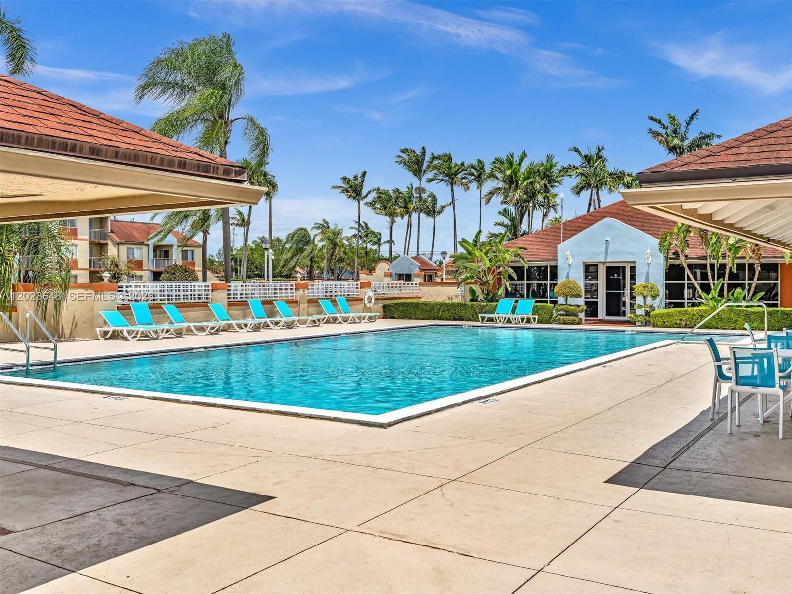 A rectangular swimming pool is surrounded by a concrete deck, lounge chairs, and palm trees — 18850 NW 57th Ave # 208, Hialeah FL 33015, HIALEAH, FL