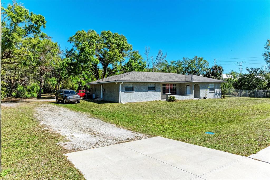 A single-story house with a gray stucco exterior and a gravel driveway sits on grass — 4007 45TH STREET E, BRADENTON, FL