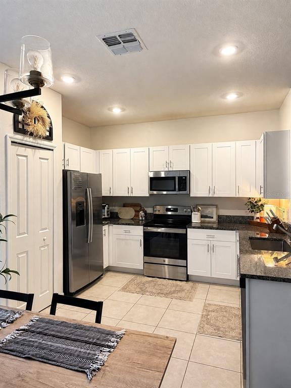 A kitchen features white cabinets, stainless steel appliances, dark granite countertops, and tile flooring — 21161 THREADFIN WAY, LAND O LAKES, FL