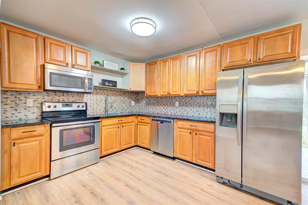A kitchen features light wood cabinets, stainless steel appliances, a tiled backsplash, and wood-look flooring — 813 7TH STREET, MERRITT ISLAND, FL