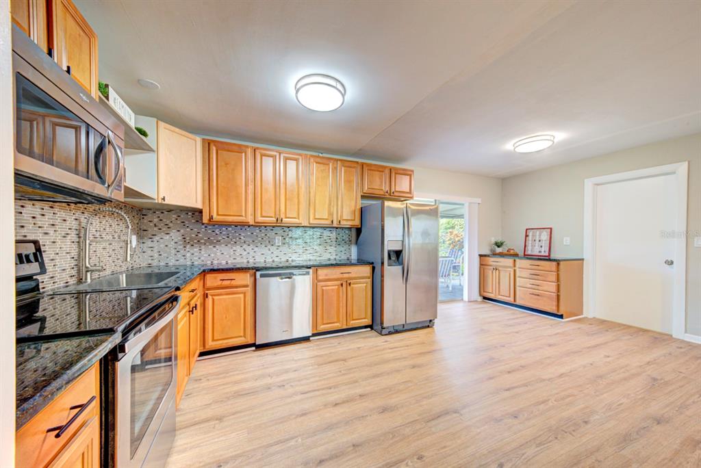 A kitchen features light wood cabinets, stainless steel appliances, a tiled backsplash, and wood-look flooring — 813 7TH STREET, MERRITT ISLAND, FL