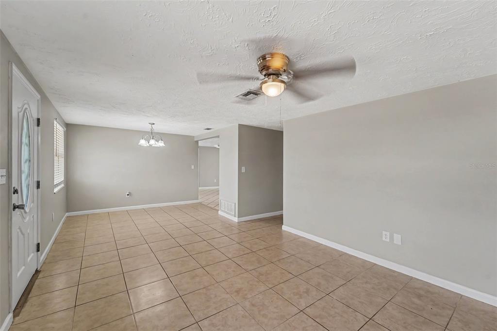 An open-concept living and dining area features light gray walls and beige tile flooring — 3344 TRASK DRIVE, HOLIDAY, FL