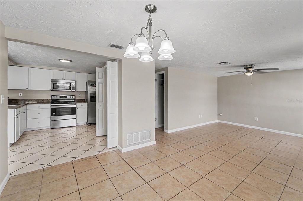 A kitchen with white cabinets and stainless steel appliances opens into a tiled dining area — 3344 TRASK DRIVE, HOLIDAY, FL