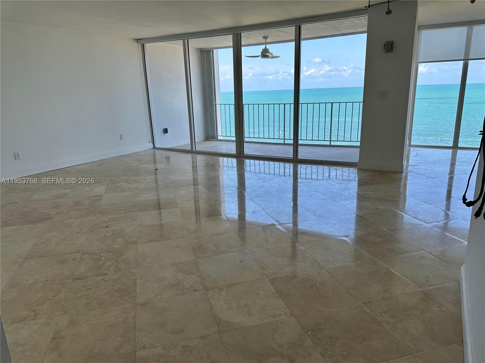 An empty room with beige tile flooring features floor-to-ceiling windows overlooking the ocean — 881 Ocean Dr # 10D, Key Biscayne FL 33149, KEY BISCAYNE, FL