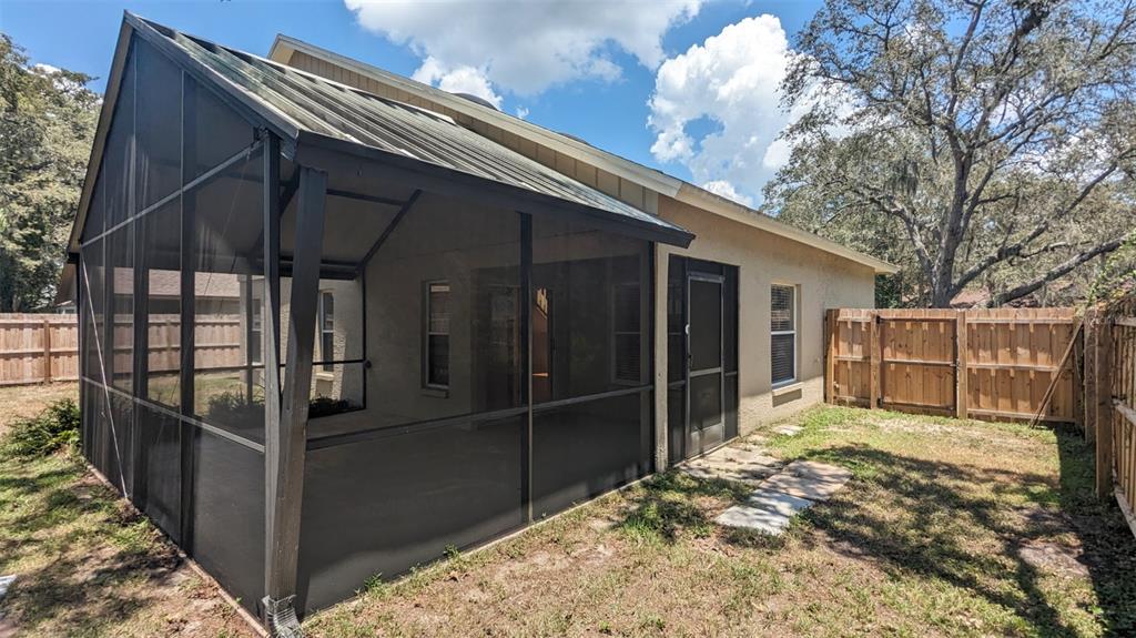 A screened-in patio with a metal roof sits adjacent to a fenced backyard — 4029 QUAIL BRIAR DRIVE, VALRICO, FL