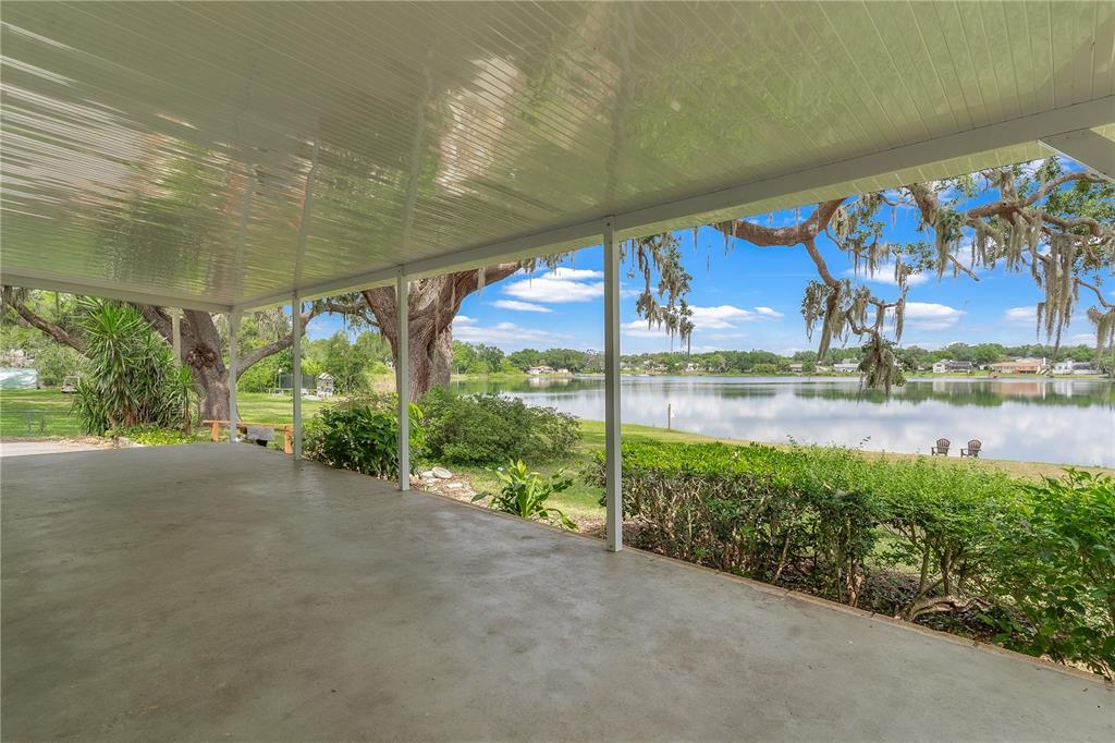 A covered concrete patio overlooks a lake with large trees and a grassy yard — 1451 OSCEOLA AVENUE, TAVARES, FL
