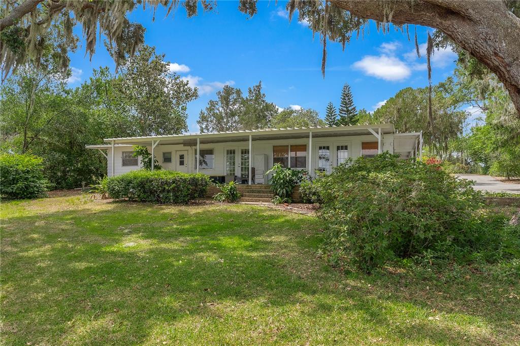 A white single-story house with a covered porch sits on a grassy lot with trees — 1451 OSCEOLA AVENUE, TAVARES, FL