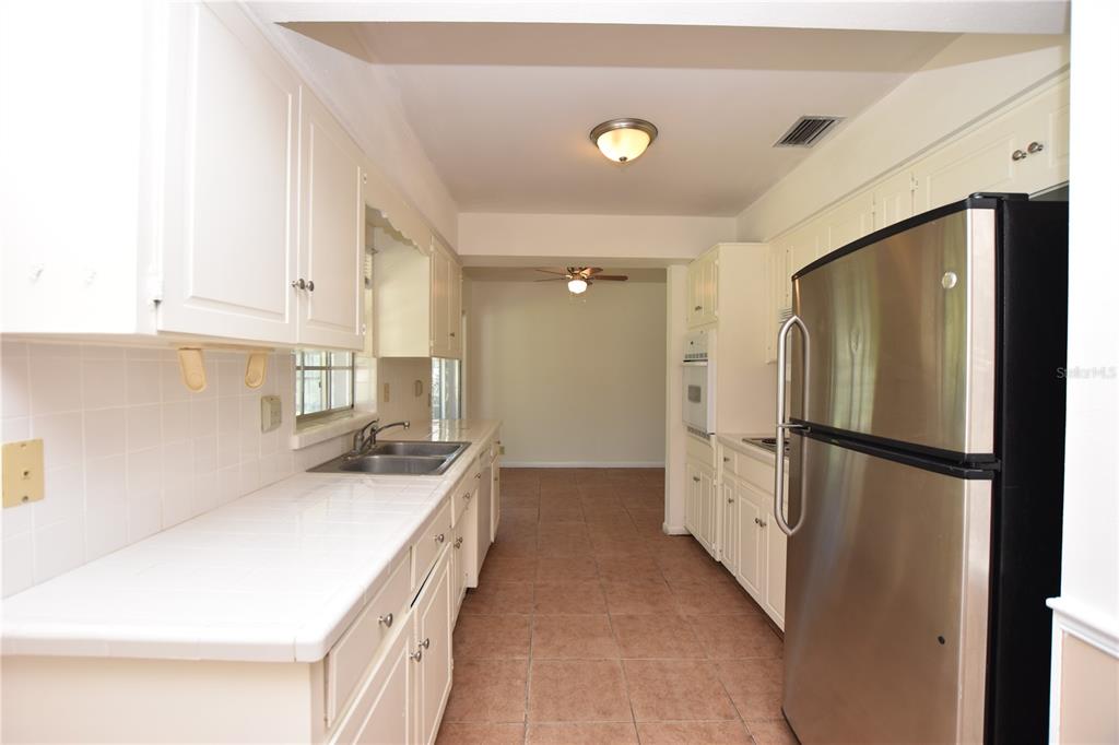 A kitchen with white cabinets, tiled countertops, and a stainless steel refrigerator — 204 CHAUCER LANE, WINTER HAVEN, FL