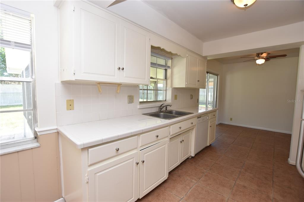 A kitchen features white cabinets, tiled countertops, and tile flooring, opening into a dining area — 204 CHAUCER LANE, WINTER HAVEN, FL