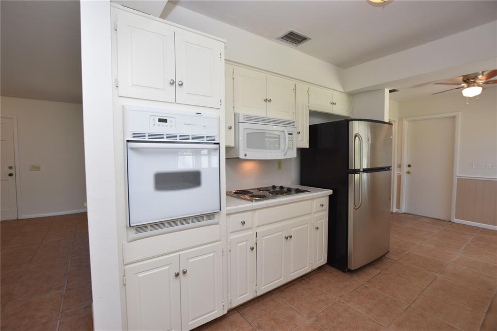 A kitchen features white cabinets, a wall oven, a cooktop, and a stainless steel refrigerator — 204 CHAUCER LANE, WINTER HAVEN, FL