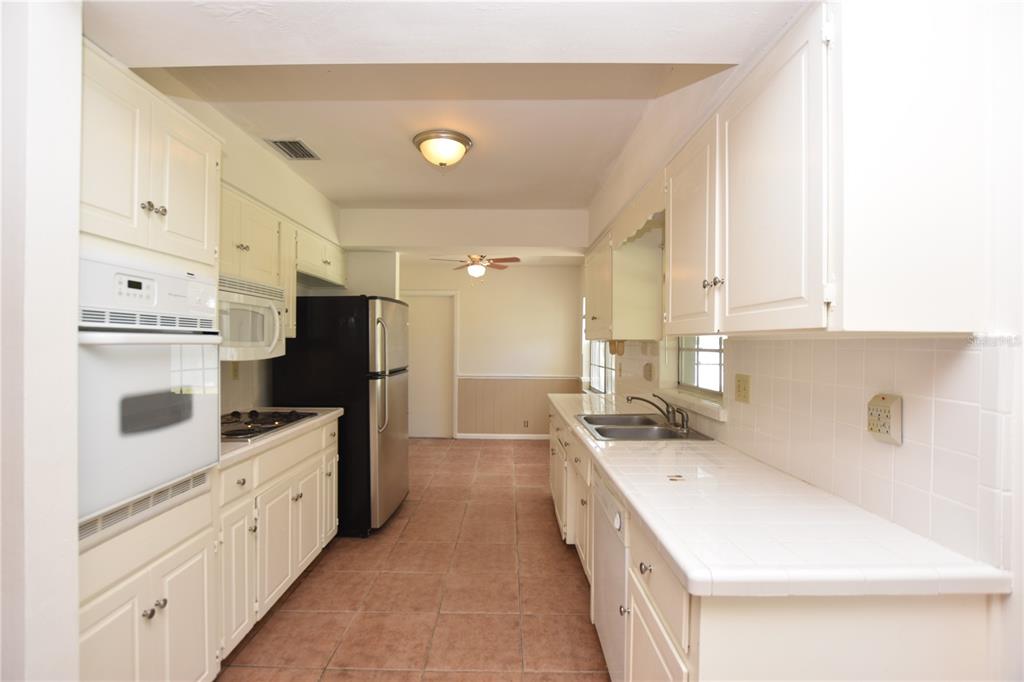 A galley-style kitchen features white cabinets, tile countertops, a black refrigerator, and tile flooring — 204 CHAUCER LANE, WINTER HAVEN, FL
