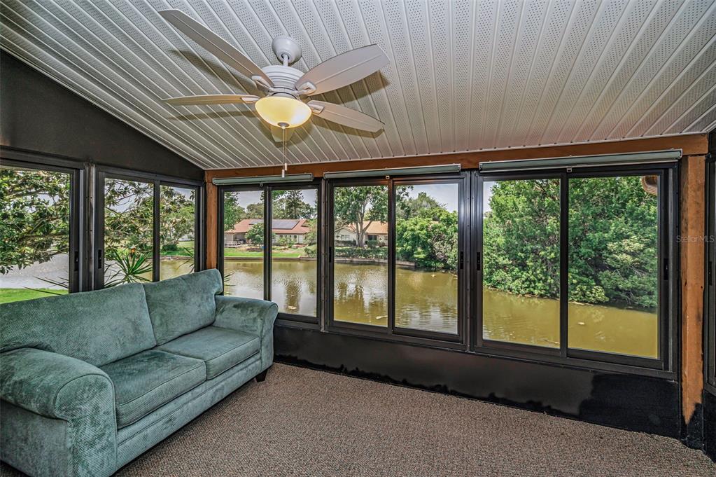 A sunroom features a ceiling fan, gray carpeting, black window frames, and views of water — 3835 LIGHTHOUSE WAY, NEW PORT RICHEY, FL