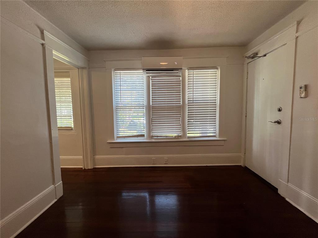 A room with dark hardwood floors, white walls, a triple window, and a wall-mounted AC unit — 510 E JACKSON ST UNIT 2, ORLANDO, FL