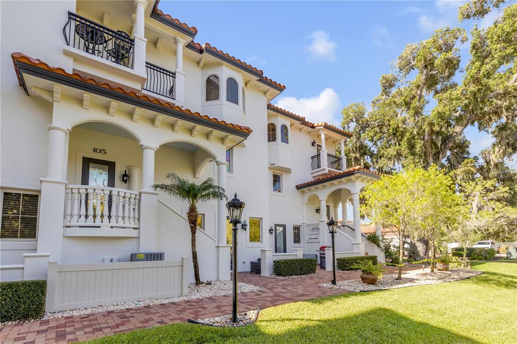 The exterior of a multi-story white stucco building features balconies, arched windows, and brick walkways — 5090 RIVERSIDE DRIVE UNIT 105, PORT ORANGE, FL