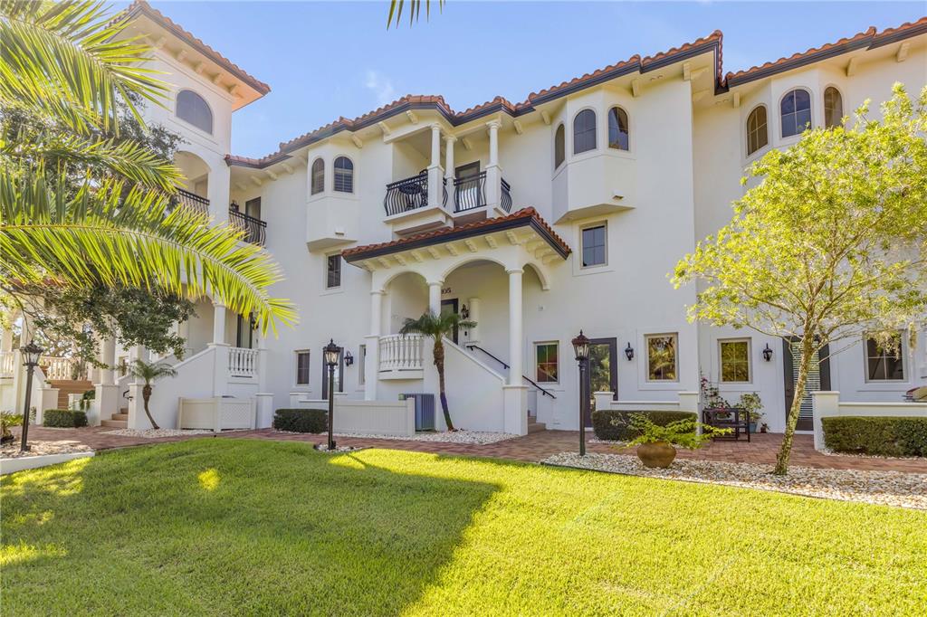 A multi-story white stucco building with arched windows, balconies, and a paved patio area — 5090 RIVERSIDE DRIVE UNIT 105, PORT ORANGE, FL