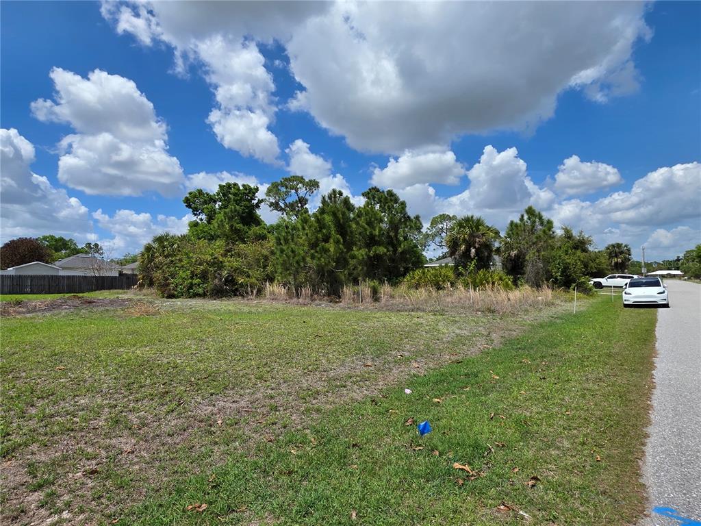 A vacant, grassy residential lot with trees and shrubs under a cloudy blue sky — 215 FLETCHER STREET, PORT CHARLOTTE, FL