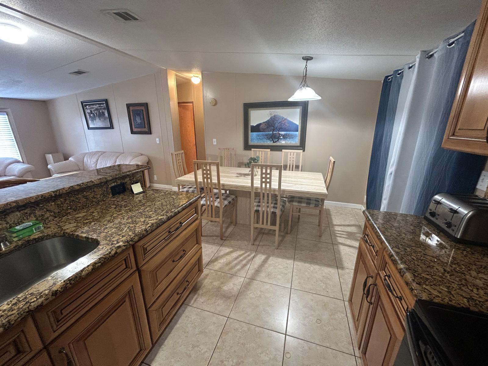 A kitchen with granite countertops and wooden cabinets overlooks a dining area with a table — 6741 NW 193rd Street, FL 32686, FL
