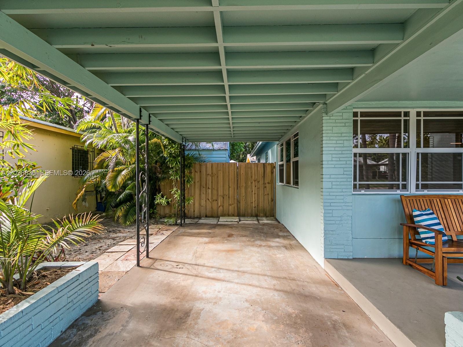 A covered concrete carport sits beside a light blue house with a wooden patio chair — 1540 Arthur St, Hollywood FL 33020, HOLLYWOOD, FL