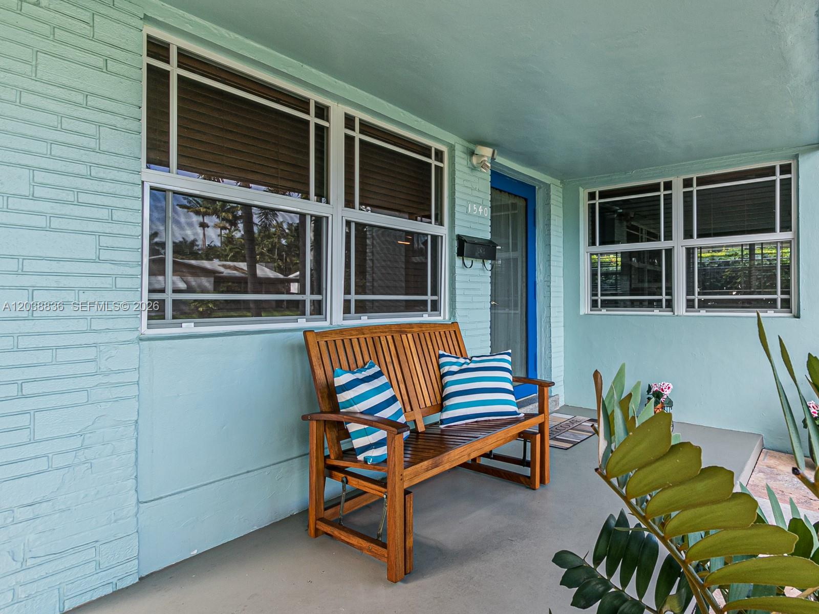 A light blue painted brick porch features a wooden bench with striped pillows and a blue door — 1540 Arthur St, Hollywood FL 33020, HOLLYWOOD, FL