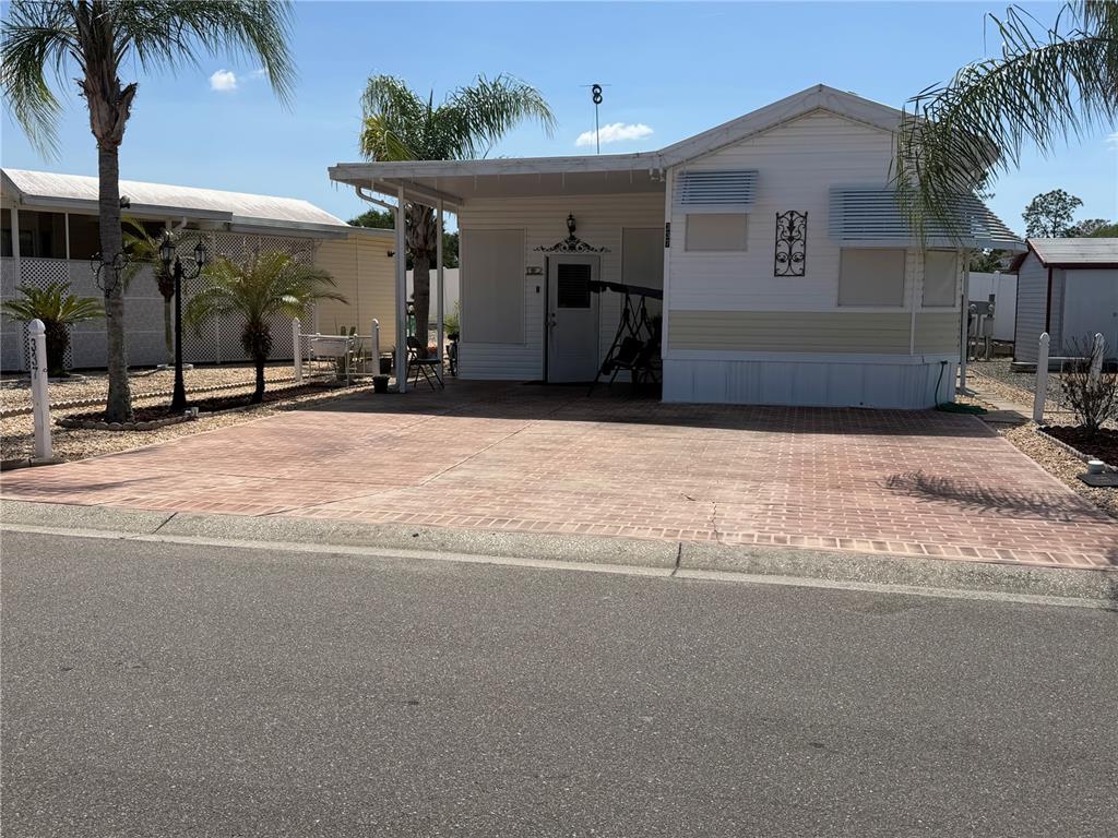 A white mobile home features a brick-paved driveway, a covered porch, and palm trees — 337 PANSY STREET, DAVENPORT, FL
