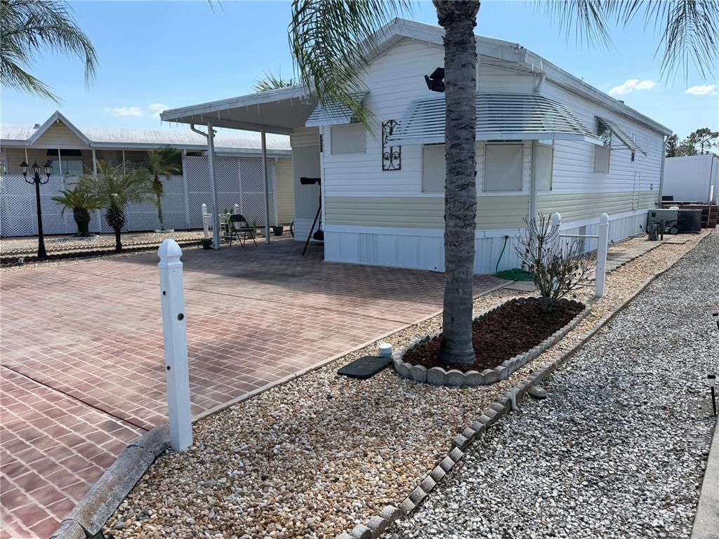A white mobile home features a brick-paved driveway, a covered patio, and a palm tree — 337 PANSY STREET, DAVENPORT, FL