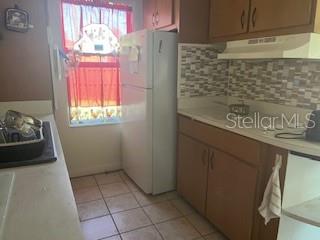 A kitchen features brown cabinets, a white refrigerator, tiled flooring, and a patterned backsplash — 2010 BLAIS AVENUE, DAYTONA BEACH, FL