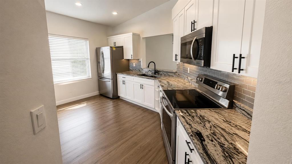 A kitchen features white cabinets, granite countertops, stainless steel appliances, and light wood-look flooring — 1712 ERIN BROOKE DRIVE, VALRICO, FL