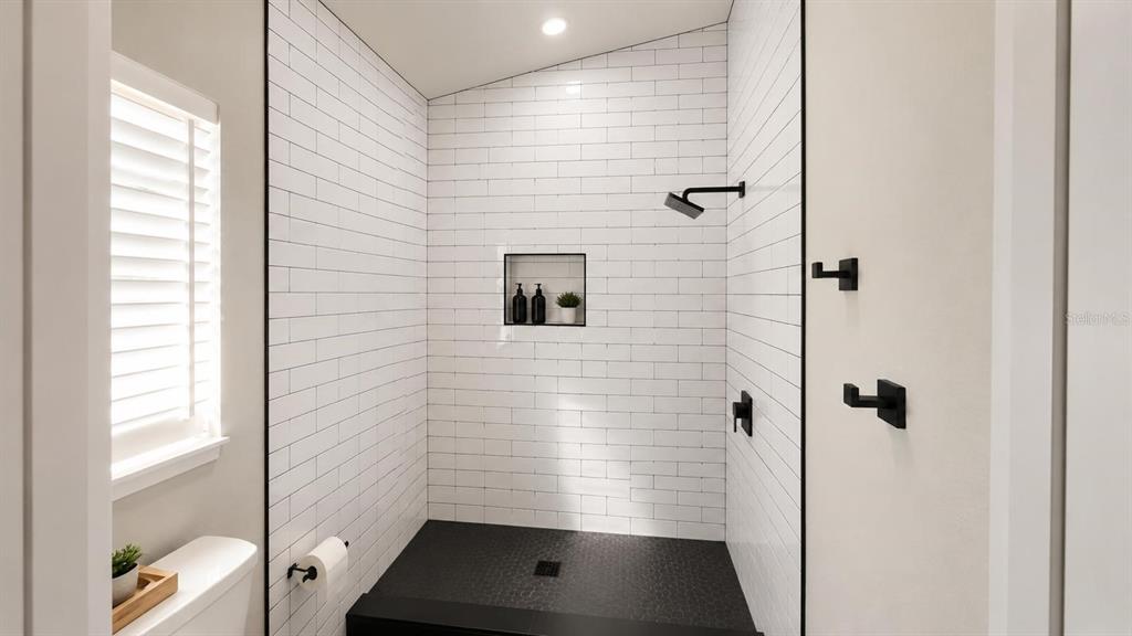 A walk-in shower features white subway tile walls, a black pebble floor, and matte black fixtures — 1712 ERIN BROOKE DRIVE, VALRICO, FL