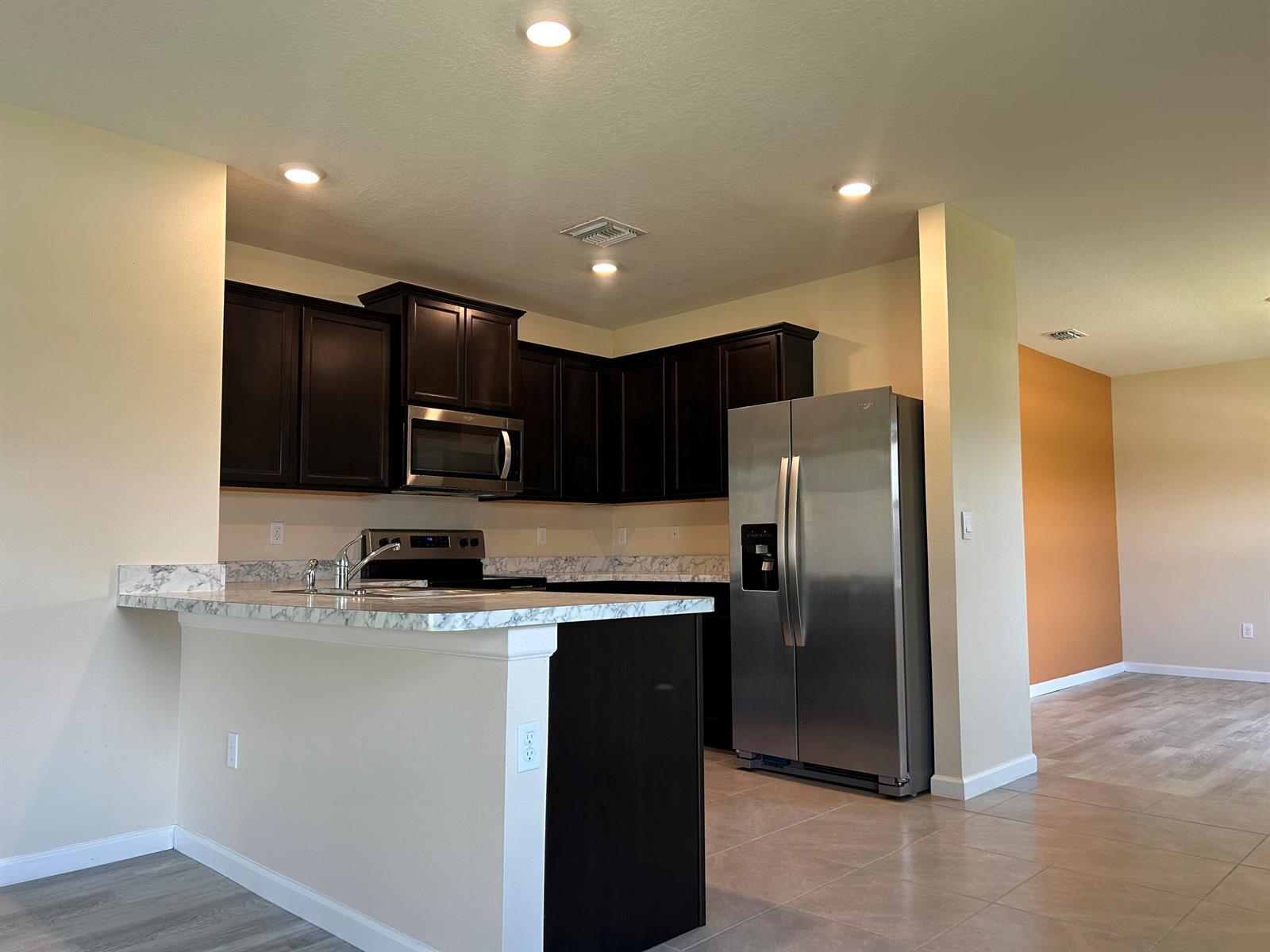 A kitchen features dark wood cabinets, stainless steel appliances, and a marble-patterned countertop island — 5414 Delight Drive, Fort Pierce FL 34947, FORT PIERCE, FL