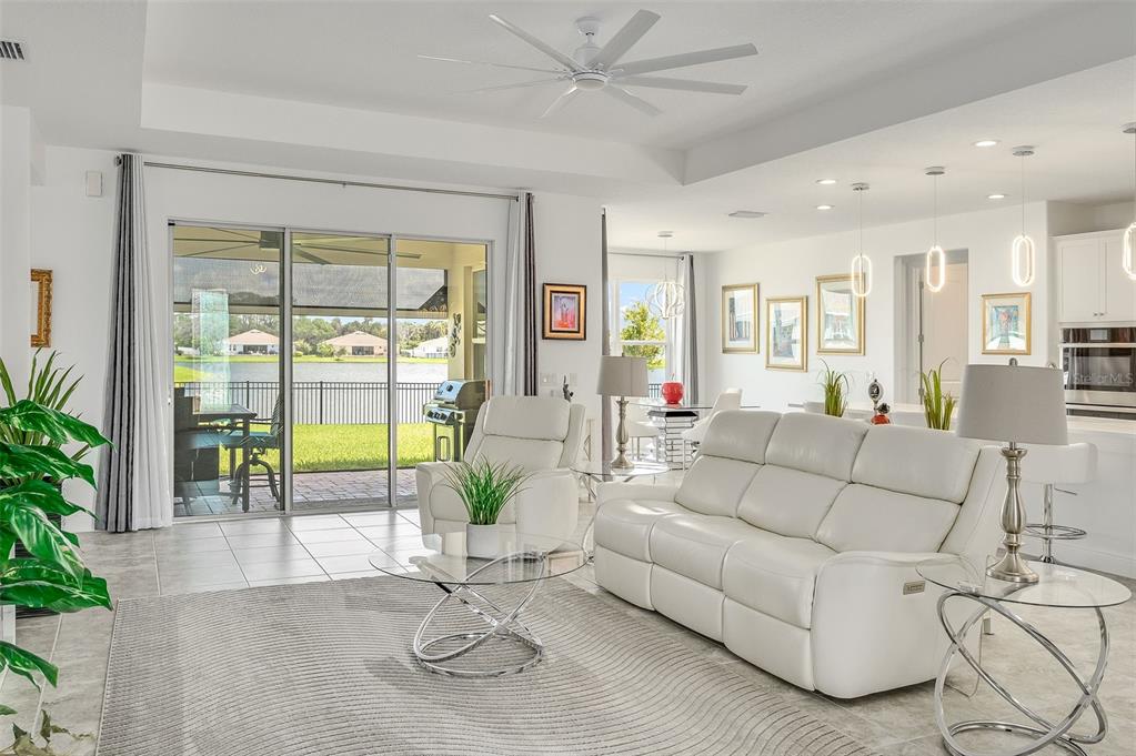 A bright living room with white leather furniture, a glass coffee table, and sliding glass doors — 375 LOYMER CIRCLE, MERRITT ISLAND, FL
