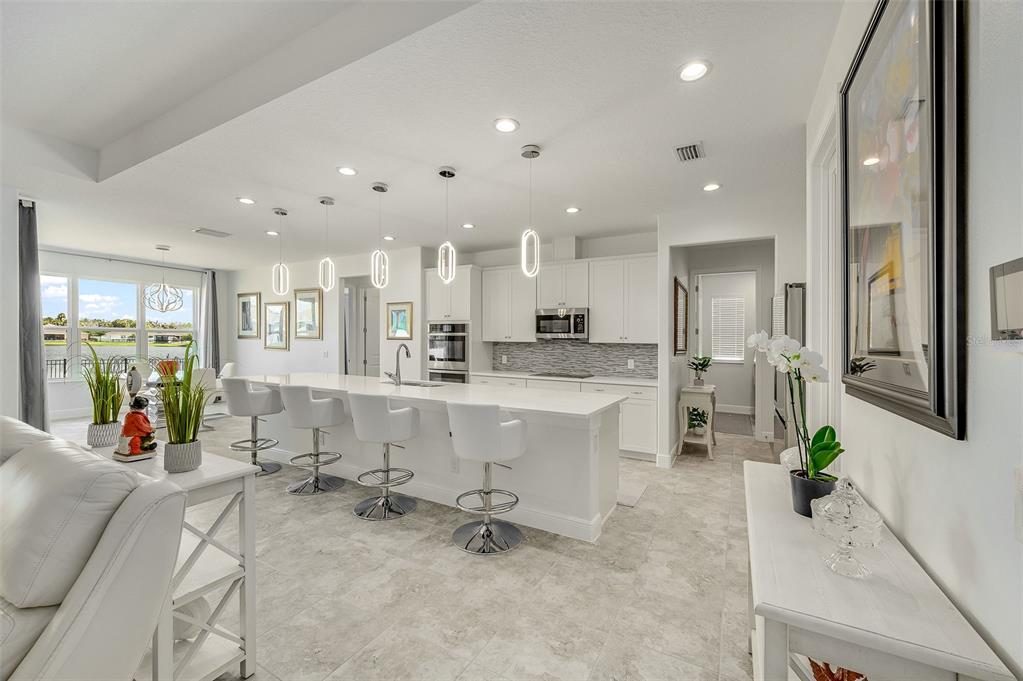 A bright, modern kitchen features a long white island with bar seating and pendant lighting — 375 LOYMER CIRCLE, MERRITT ISLAND, FL