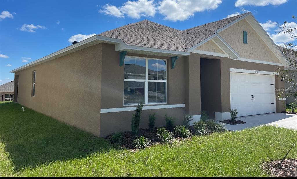 A single-story house with a tan stucco exterior, a white garage door, and a shingled roof — 1779 BUCKEYE ROAD, DAVENPORT, FL