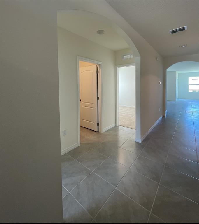A hallway with large gray floor tiles leads to an arched opening and interior rooms — 1779 BUCKEYE ROAD, DAVENPORT, FL