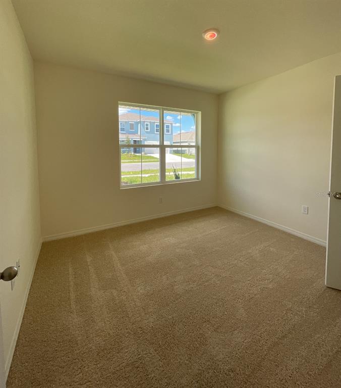 An empty bedroom features beige carpet, light-colored walls, and a window overlooking a suburban street — 1779 BUCKEYE ROAD, DAVENPORT, FL
